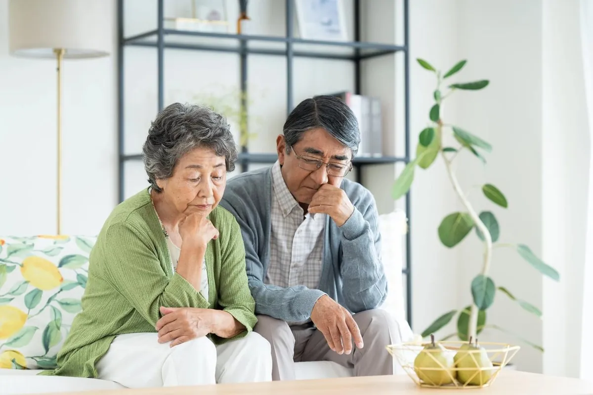 ソファで考え込む年配のご夫婦